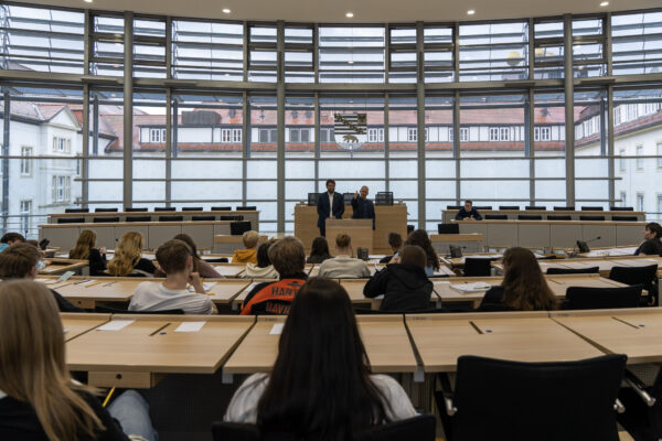 Falko Grube zusammen mit Tobias Krull im Plenarsaal des Landtags von Sachsen Anhalt am Redepult, auf den Plätzen der Abgeordneten sitzen Jugendliche