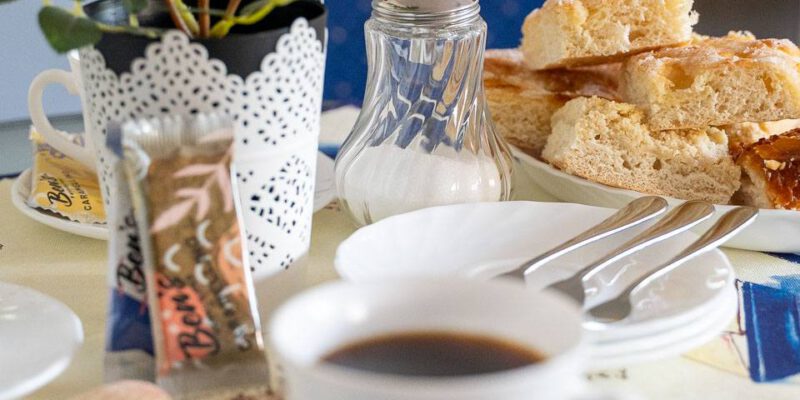 Ein hübsch gedeckter Kaffeetisch mit einer Tasse Kaffee im Vordergrund, im Hintergrund ein Teller mit Kuchenstücken